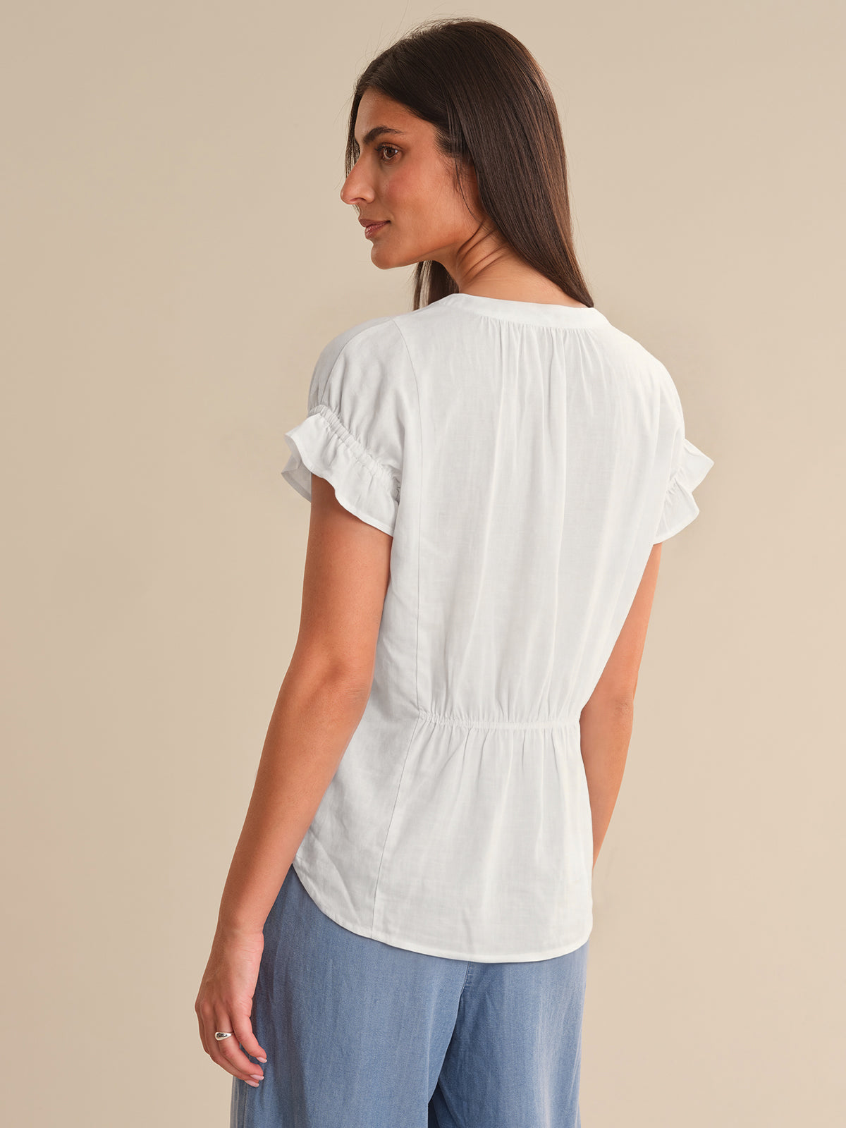 Woman wearing a white blouse with ruffled sleeves on a beige background