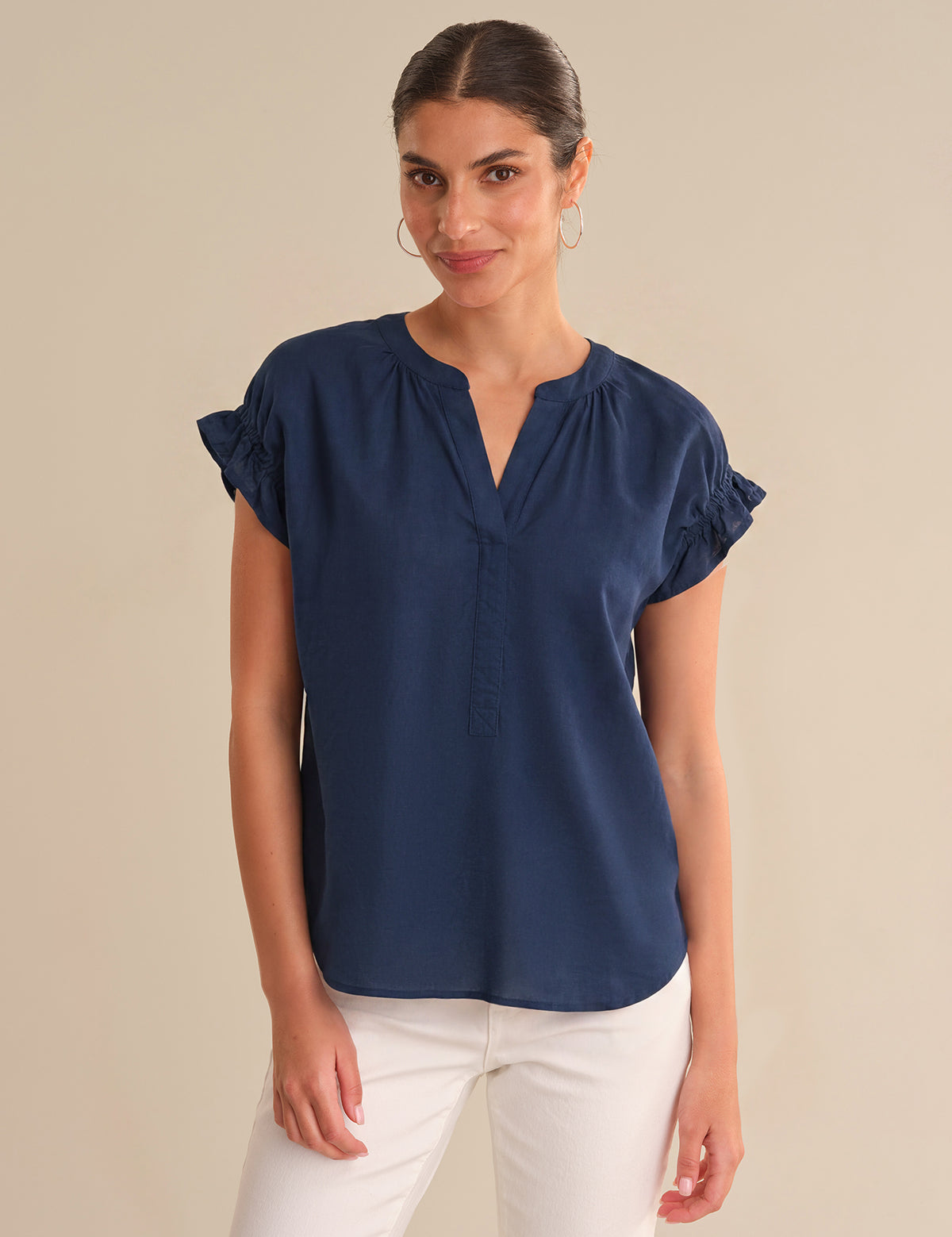 Woman wearing a navy blue blouse with ruffled sleeves on a beige background