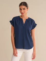Woman wearing a navy blue blouse with ruffled sleeves on a beige background