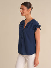 Woman wearing a navy blue blouse with ruffled sleeves on a beige background
