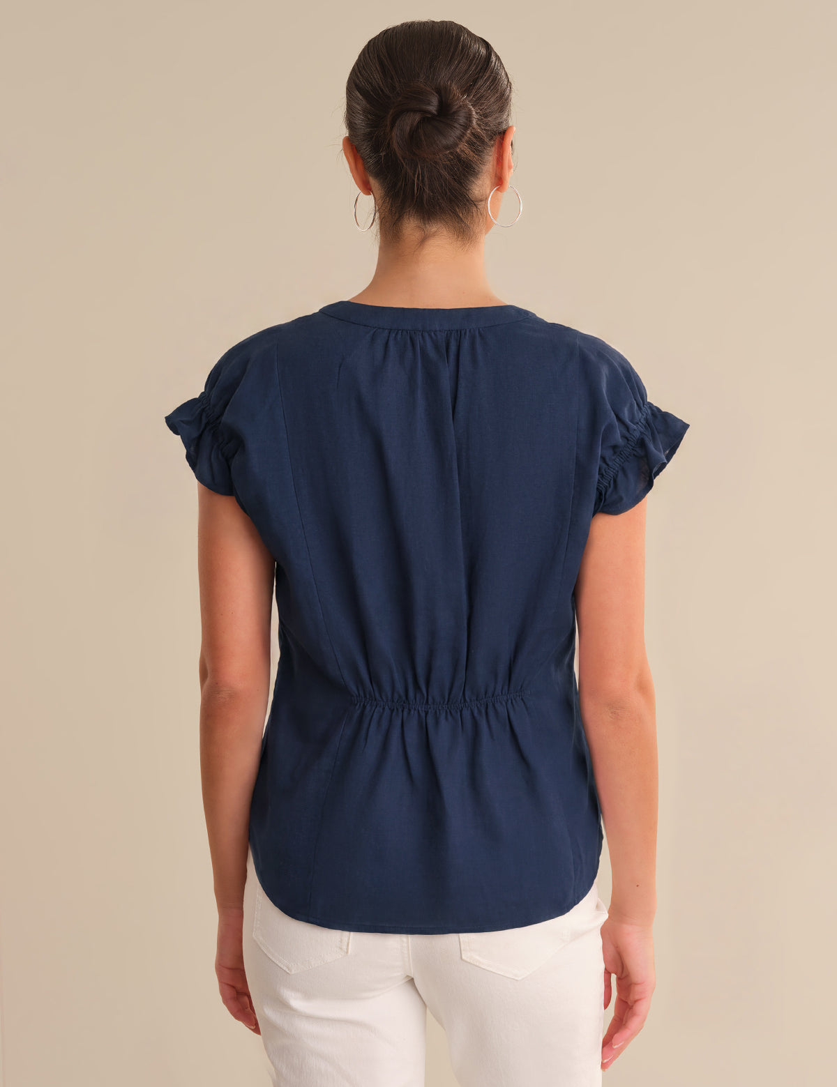 Woman wearing a navy blue blouse with ruffled sleeves on a beige background