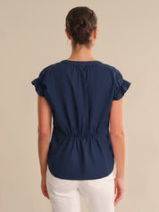 Woman wearing a navy blue blouse with ruffled sleeves on a beige background