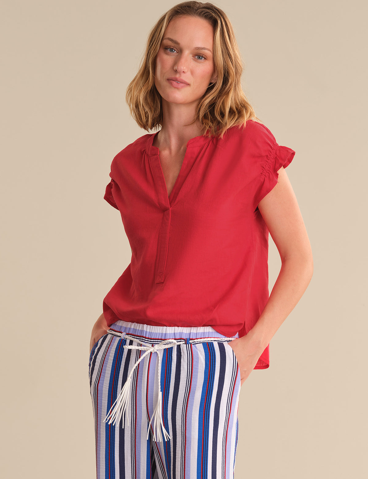 Woman wearing a red blouse and striped pants on a beige background