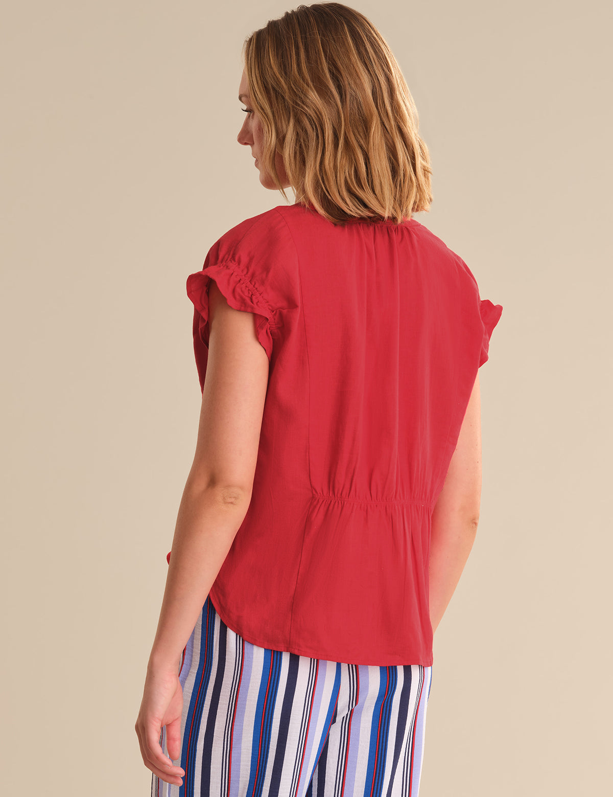 Woman wearing a red sleeveless top and striped pants on a beige background