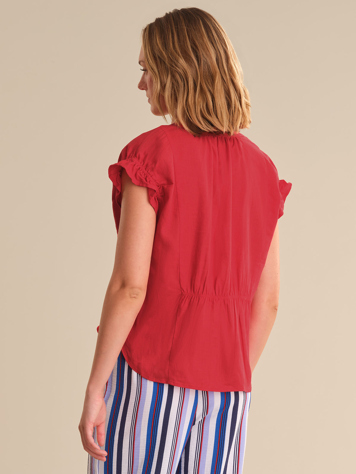 Woman wearing a red sleeveless top and striped pants on a beige background