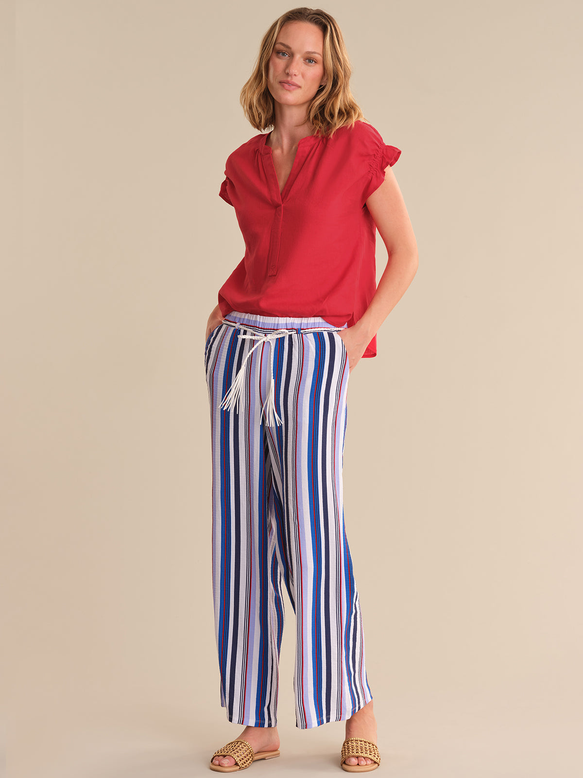 Woman wearing a red top and striped pants on a beige background