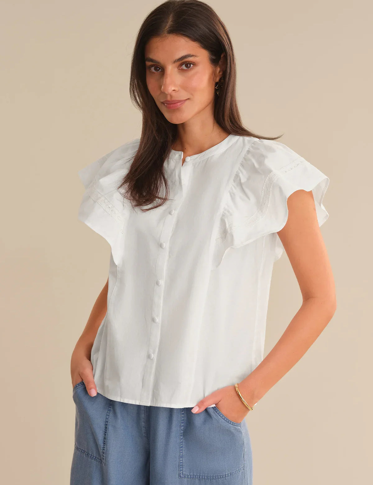 Woman wearing a white blouse with ruffled sleeves against a beige background