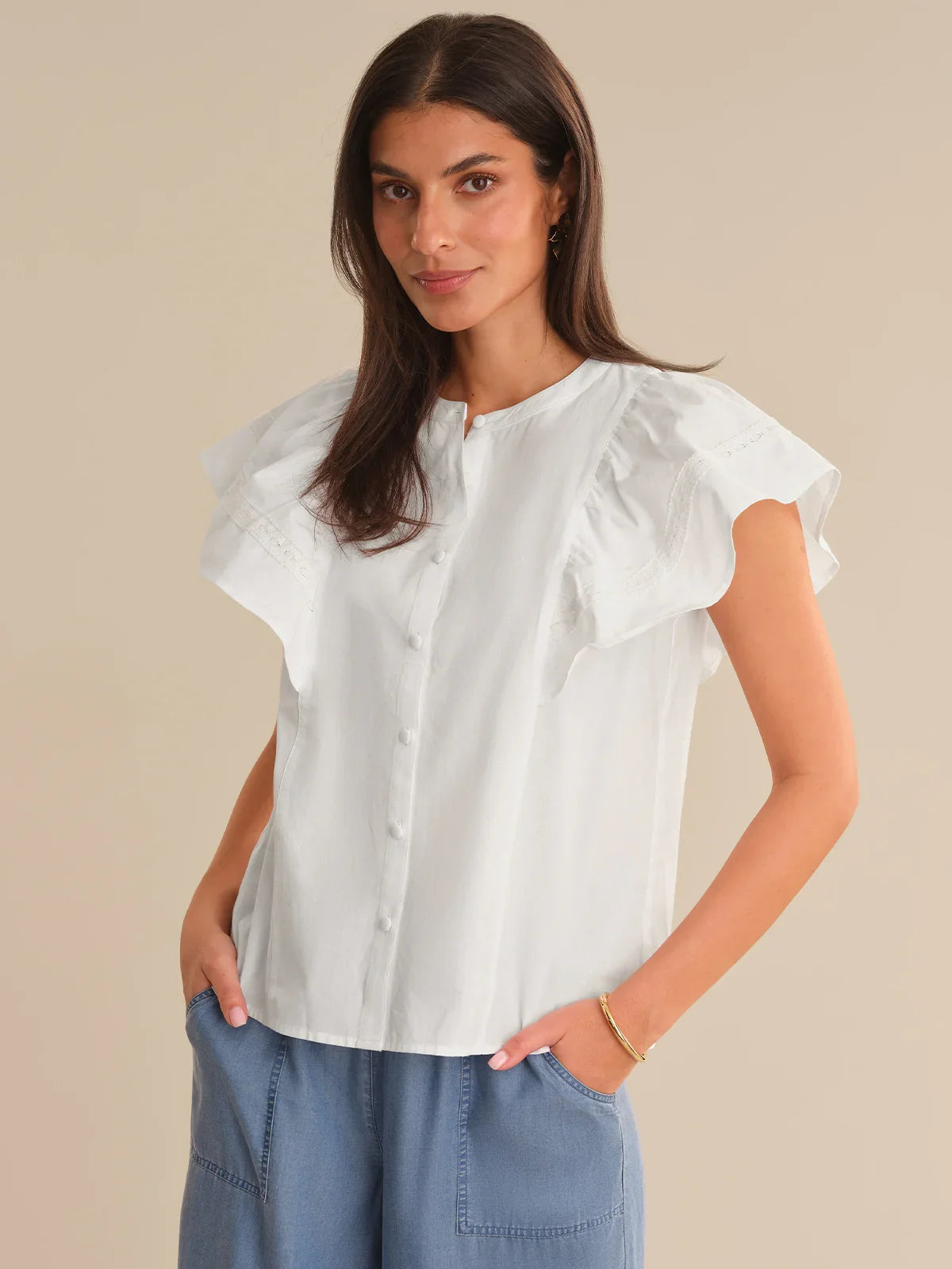Woman wearing a white blouse with ruffled sleeves against a beige background