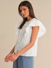 Woman wearing a light-colored blouse with ruffled sleeves against a beige background