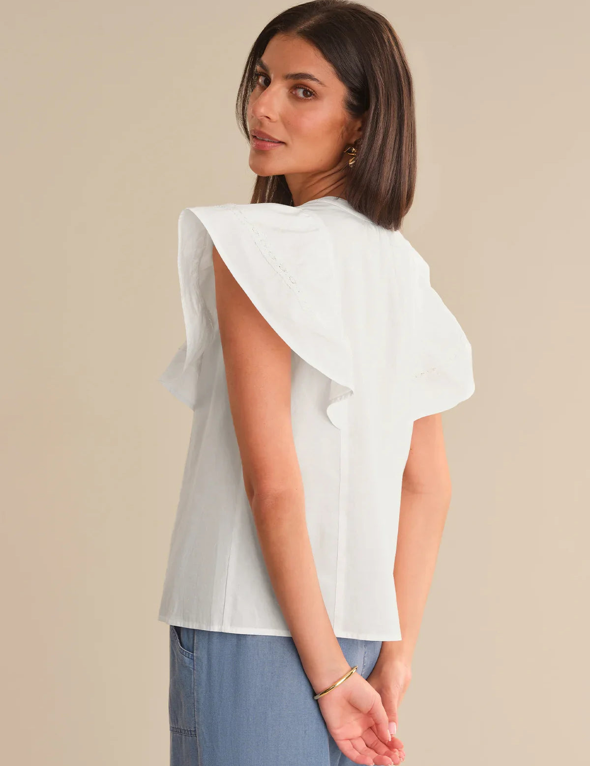 Woman wearing a white blouse with ruffled sleeves against a beige background