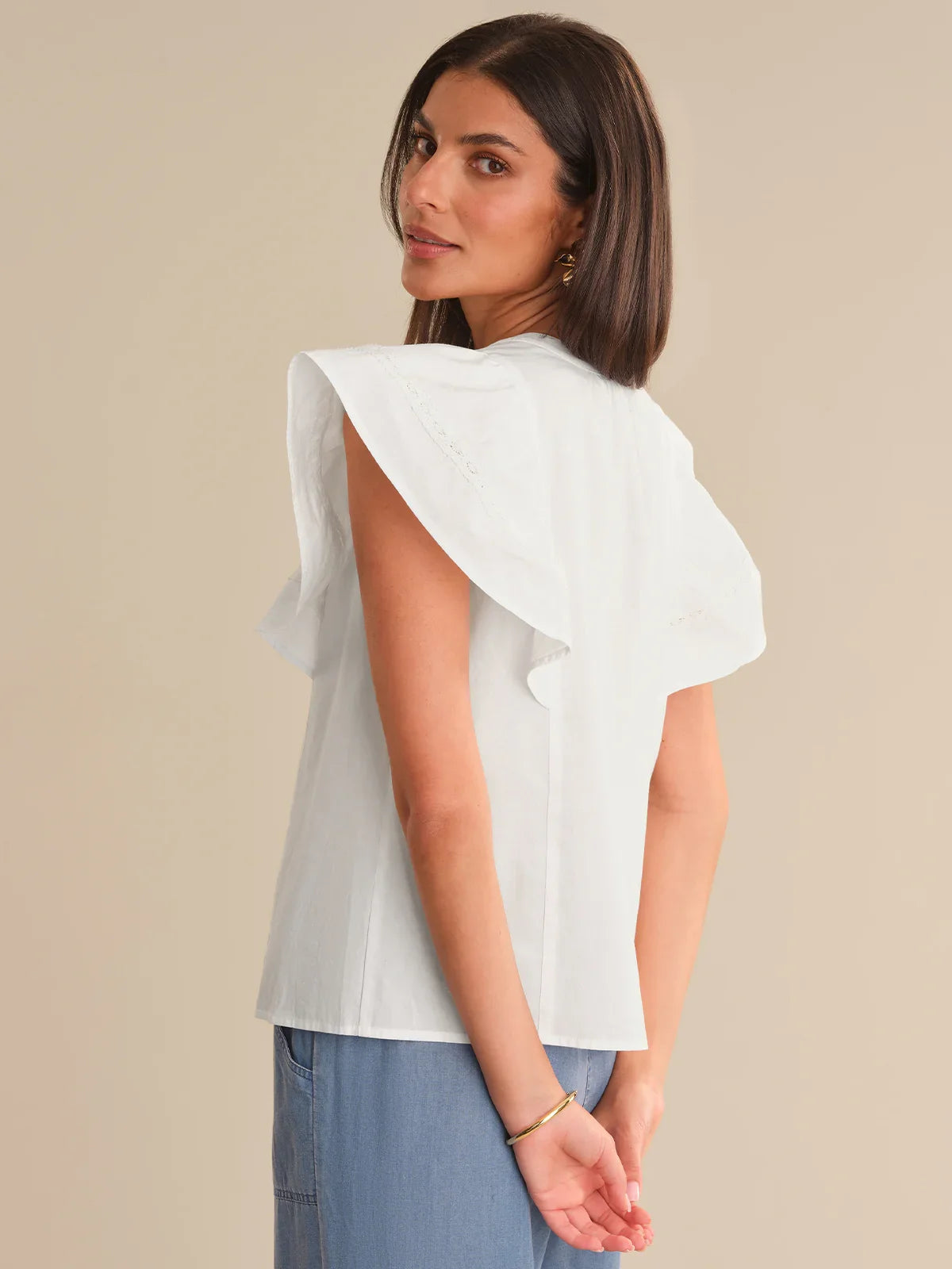 Woman wearing a white blouse with ruffled sleeves against a beige background