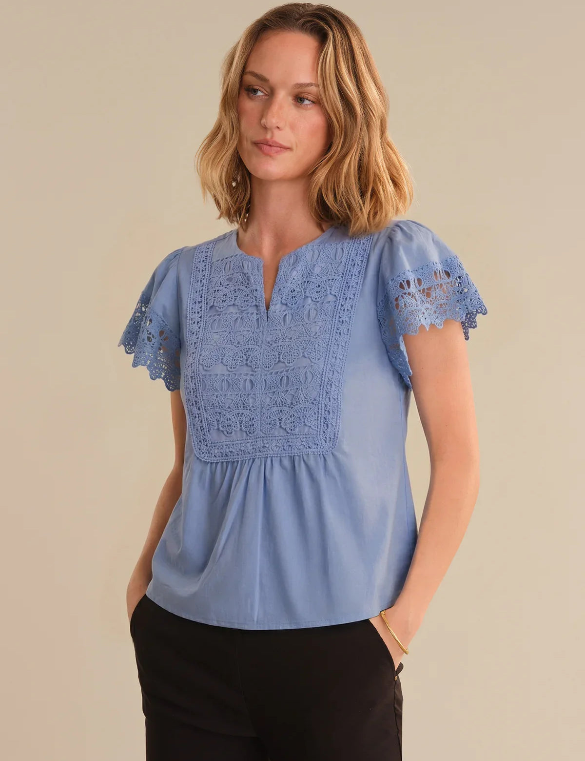 Woman wearing a blue blouse with lace details on a beige background