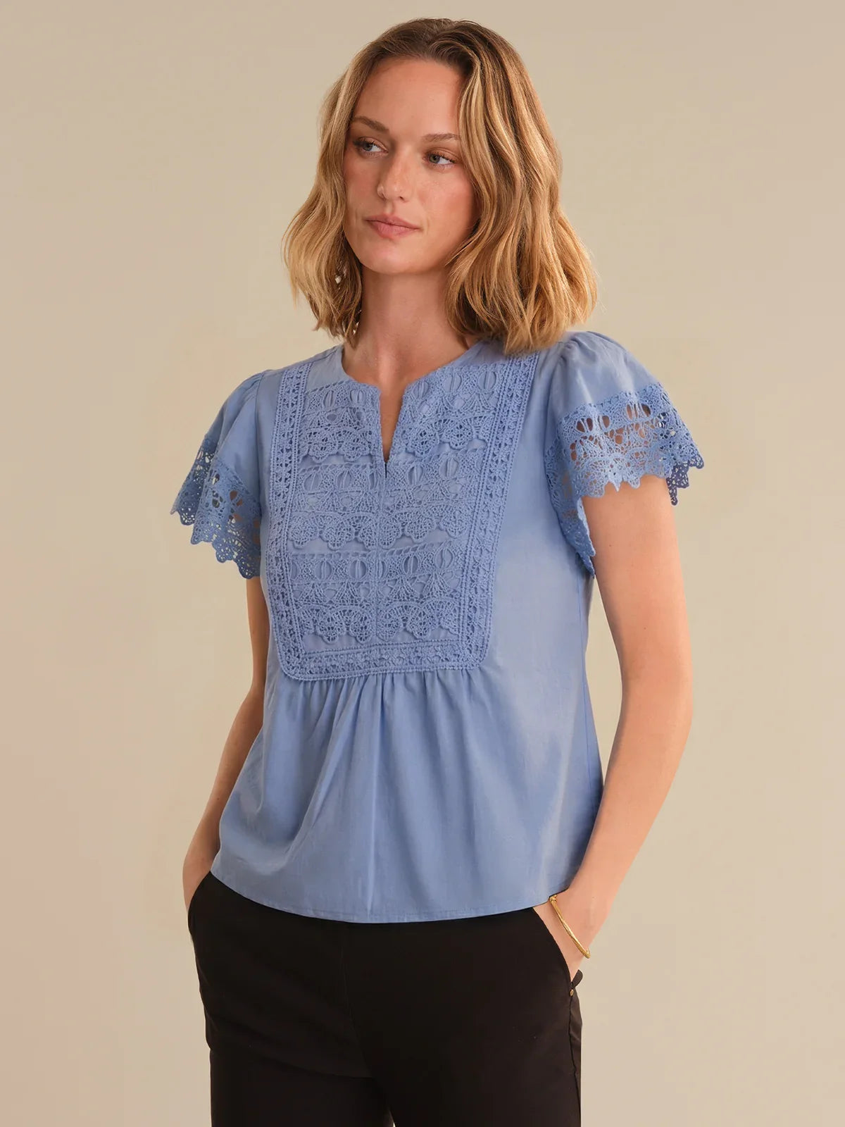Woman wearing a blue blouse with lace details on a beige background