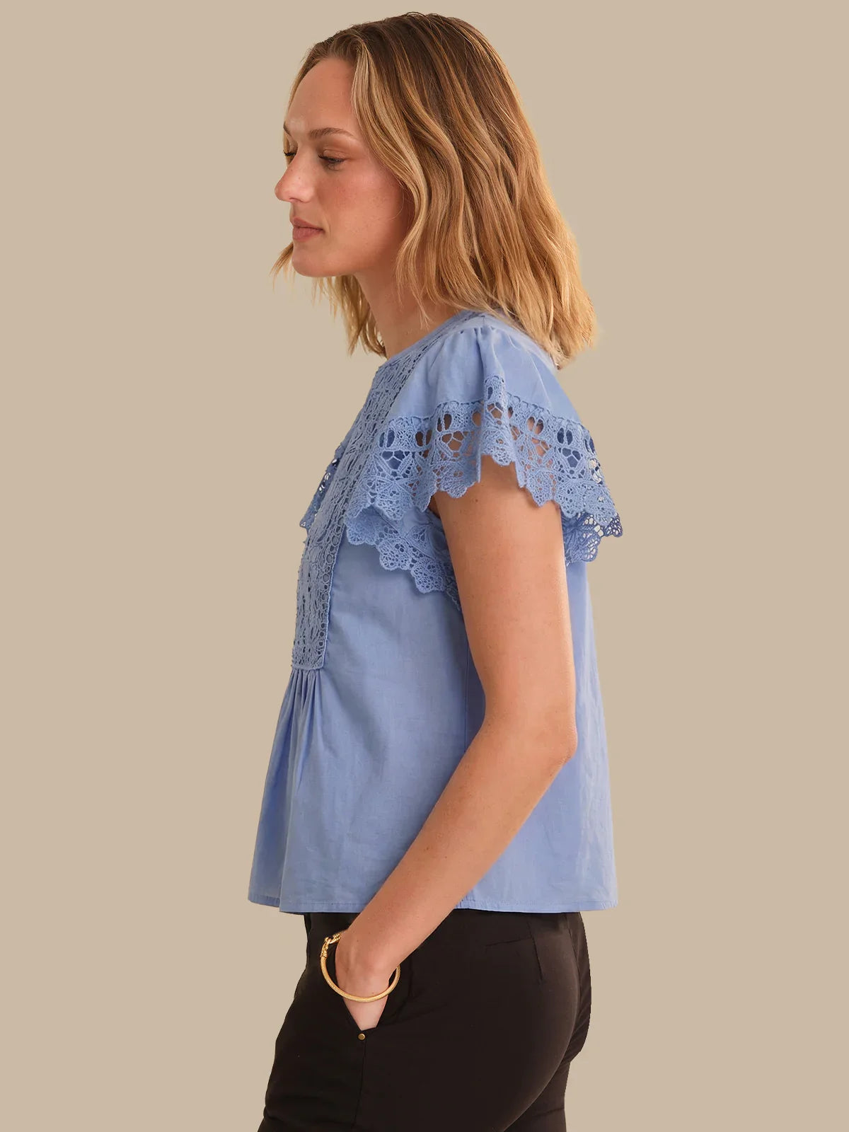 Woman wearing a light blue blouse with lace details on a beige background