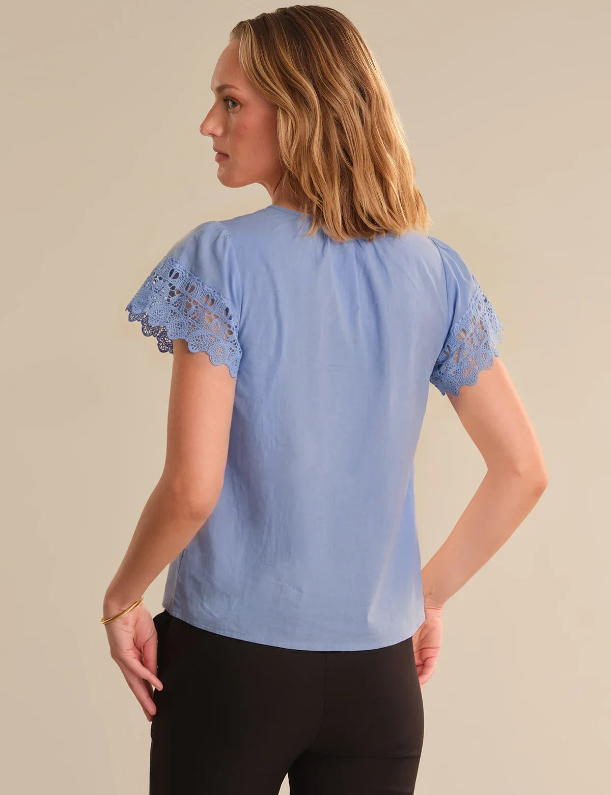 Woman wearing a light blue blouse with lace sleeves on a beige background
