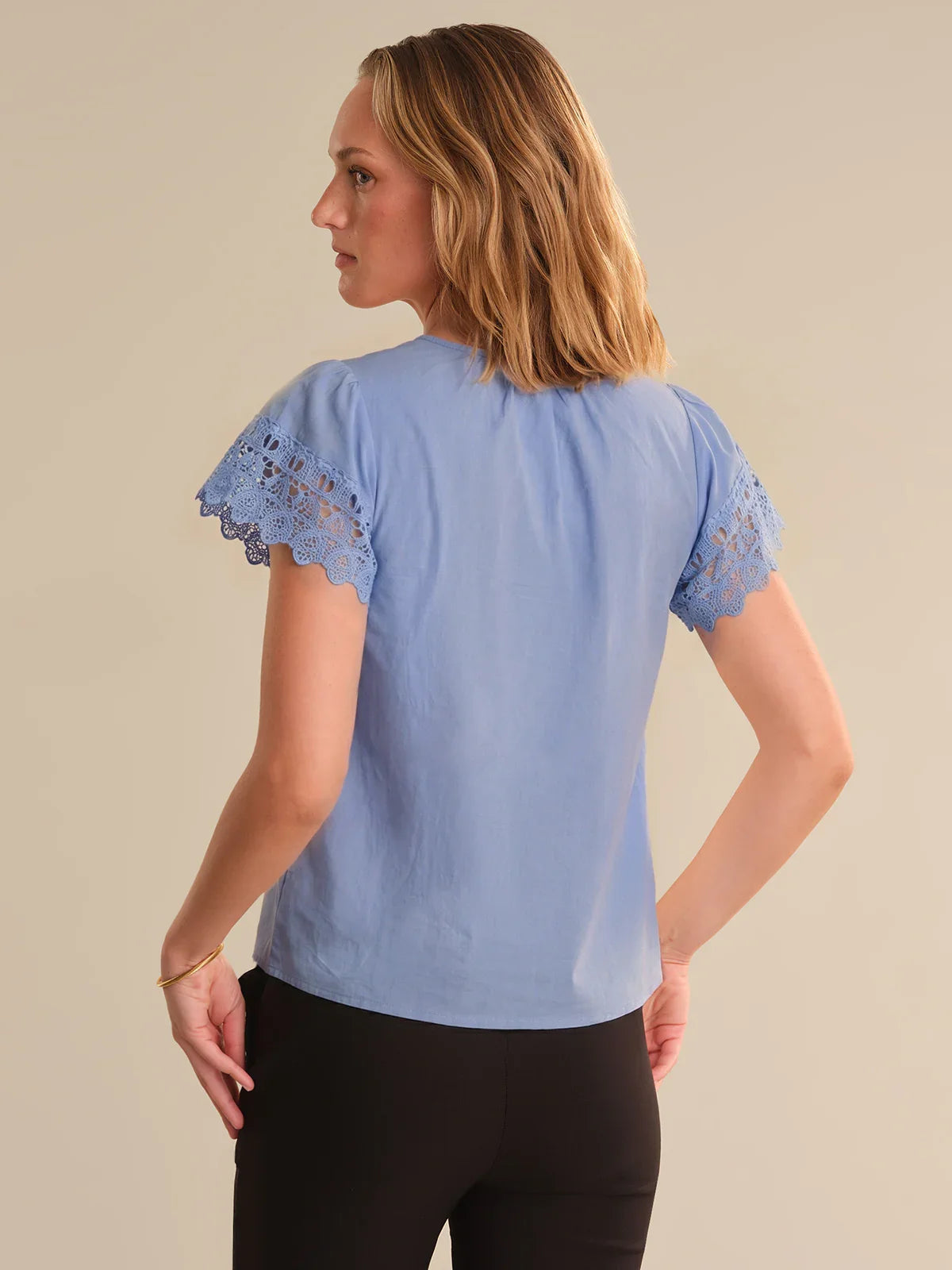 Woman wearing a light blue blouse with lace sleeves on a beige background