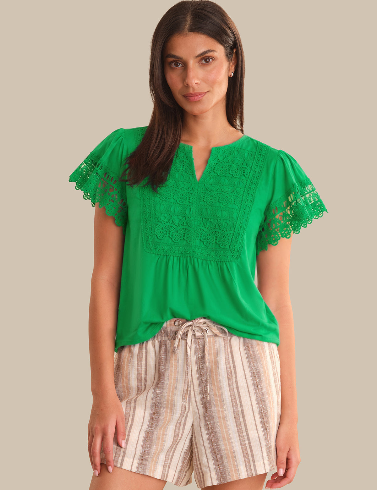 Woman wearing a green lace top and striped shorts on a beige background