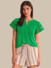 Woman wearing a green lace top and striped shorts on a beige background