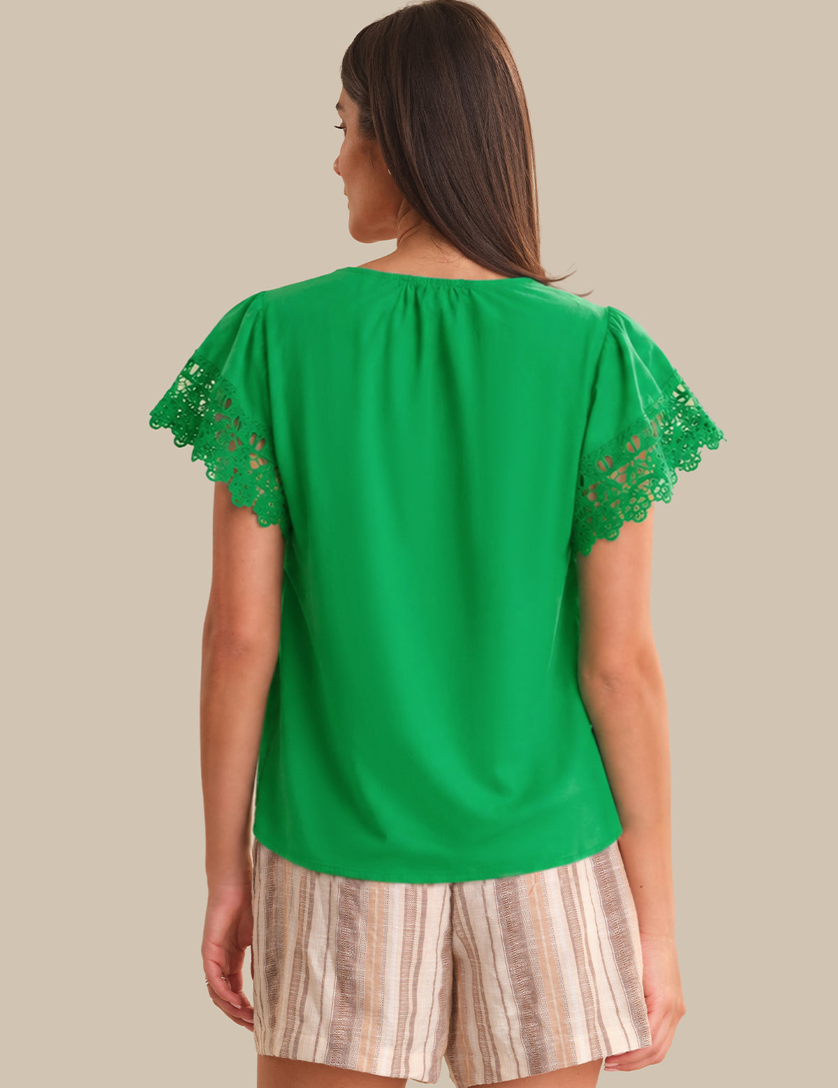 Woman wearing a green top with lace sleeves on a beige background