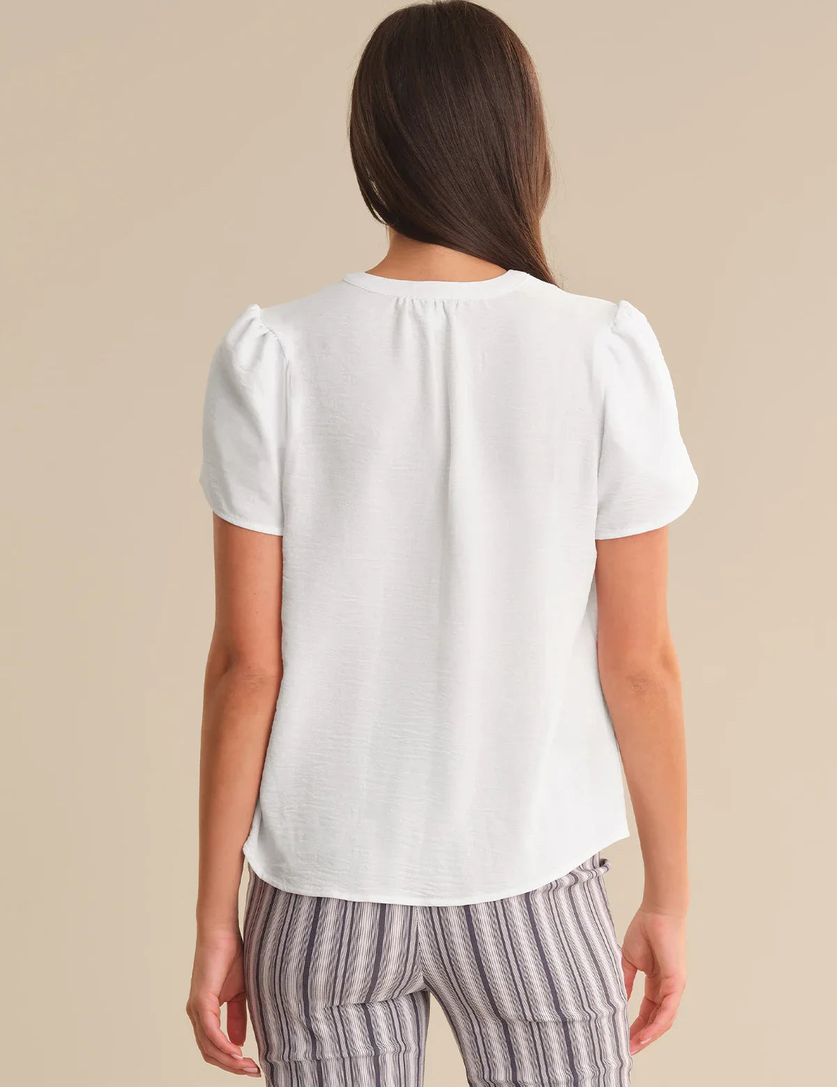 Woman wearing a white top and striped pants on a beige background