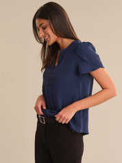 Woman wearing a blue blouse with ruffled shoulders against a beige background