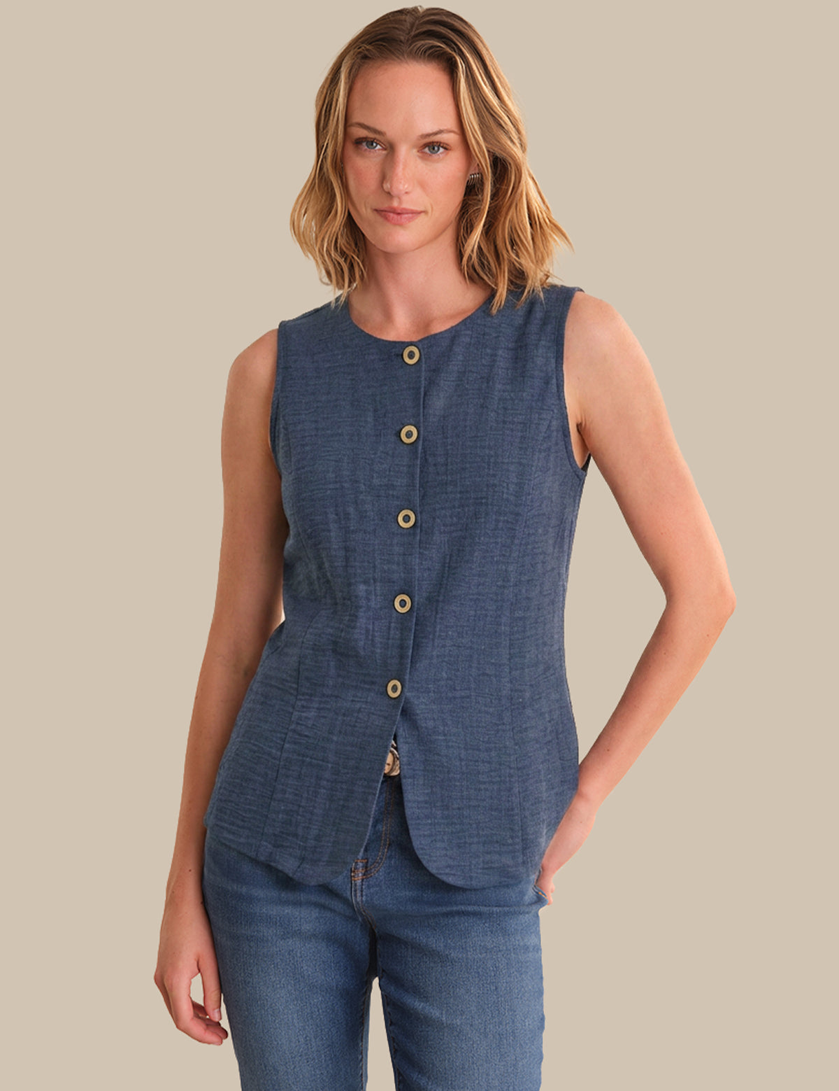 Woman wearing a blue sleeveless top with buttons on a beige background