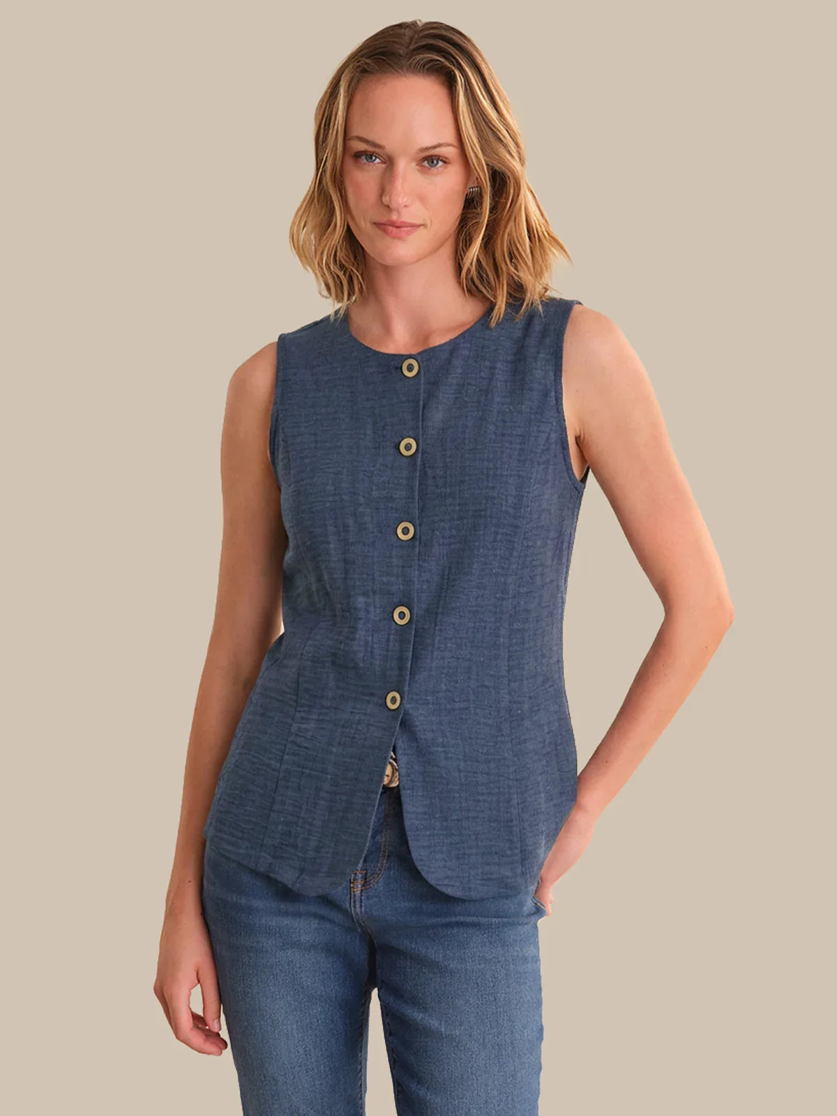 Woman wearing a blue sleeveless top with buttons on a beige background