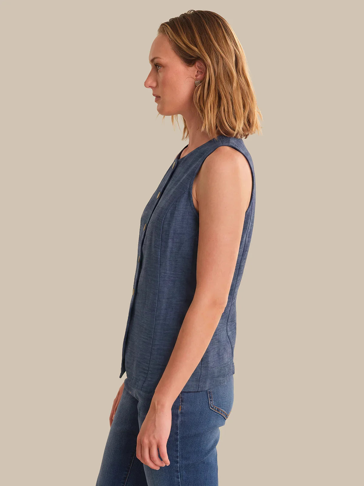 Woman wearing a blue denim vest and pants on a beige background