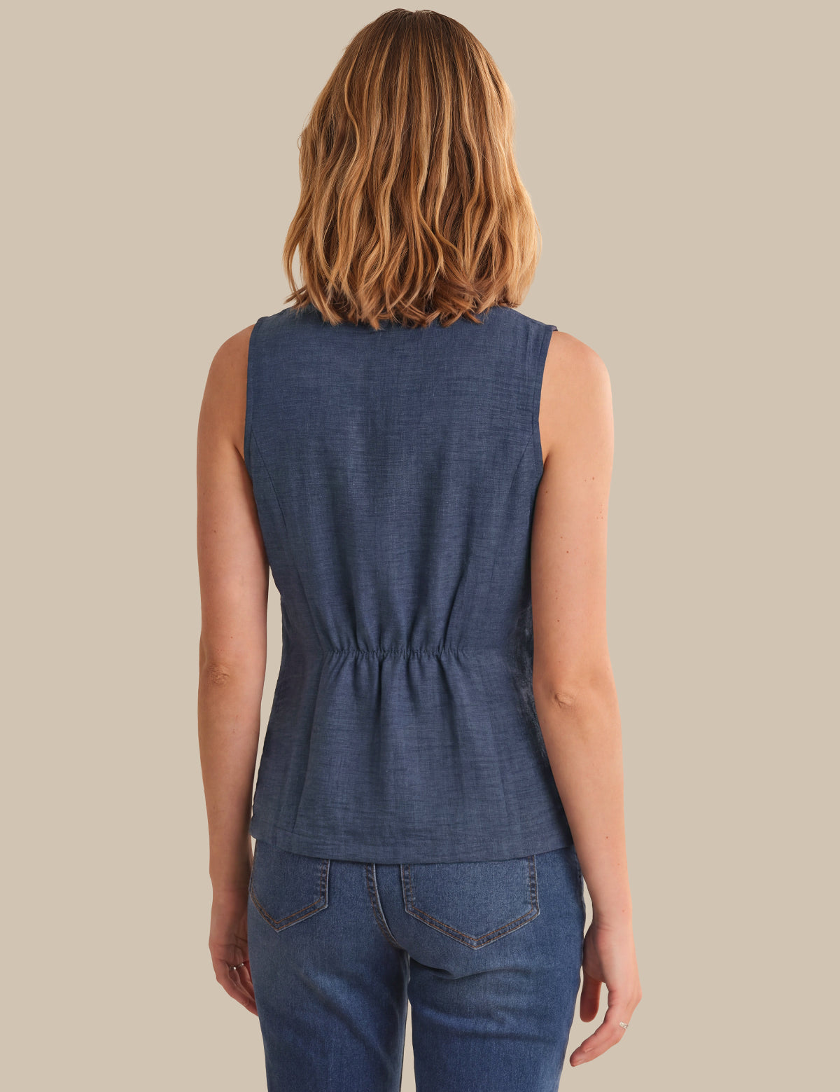 Woman wearing a blue sleeveless top and jeans on a beige background