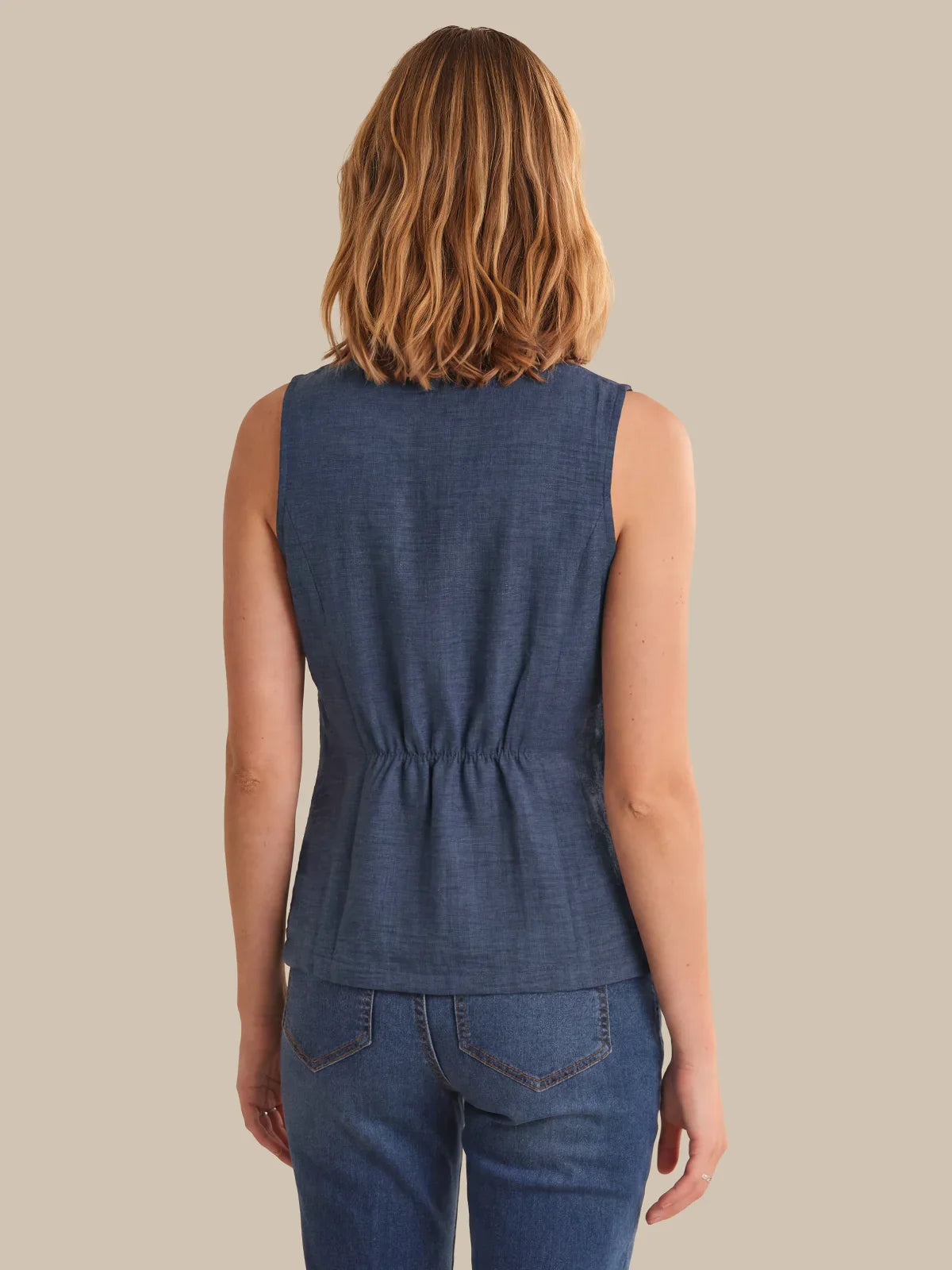 Woman wearing a blue sleeveless top and jeans on a beige background