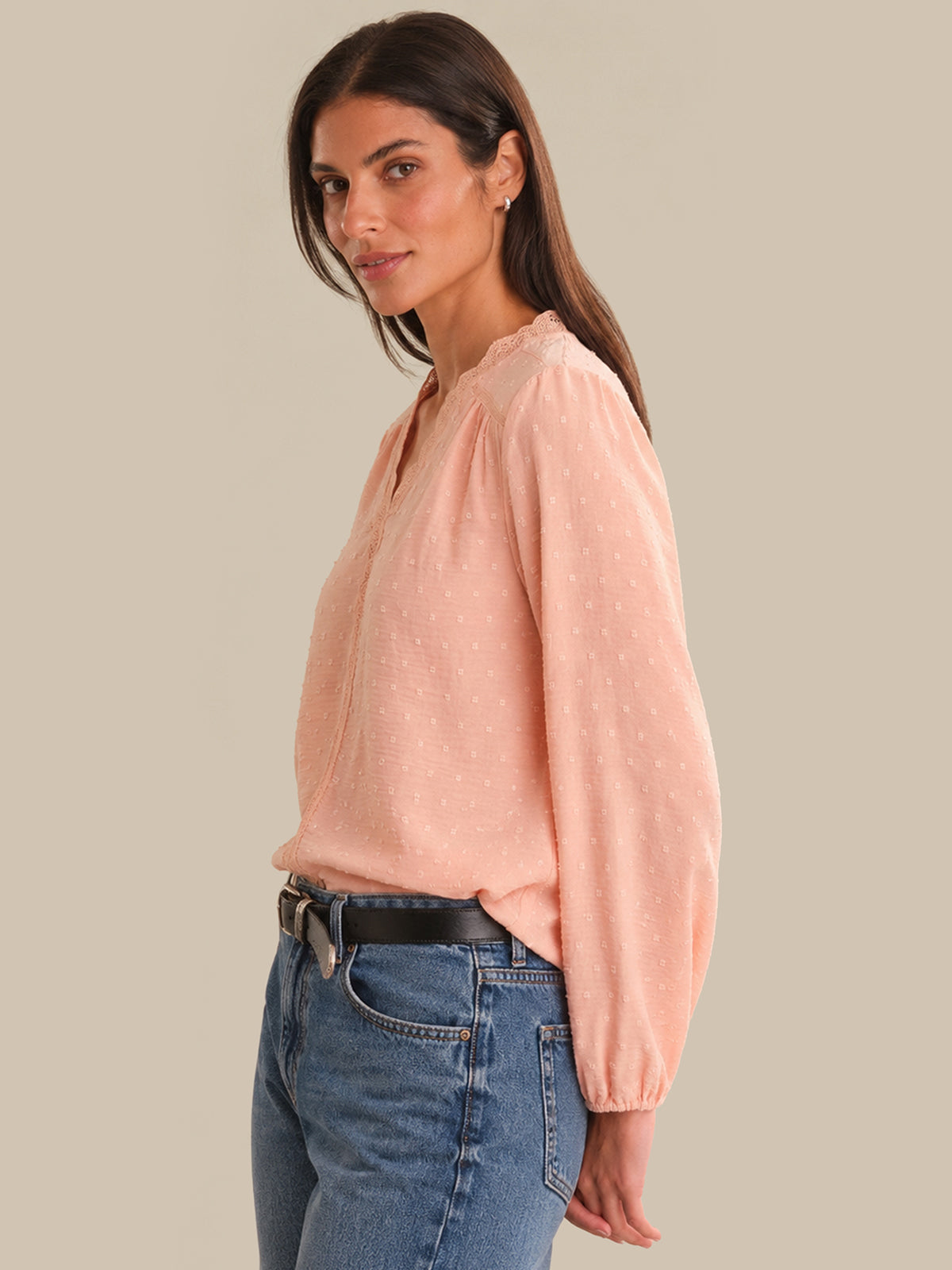 Woman wearing a light pink blouse and blue jeans against a beige background