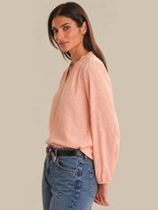 Woman wearing a light pink blouse and blue jeans against a beige background