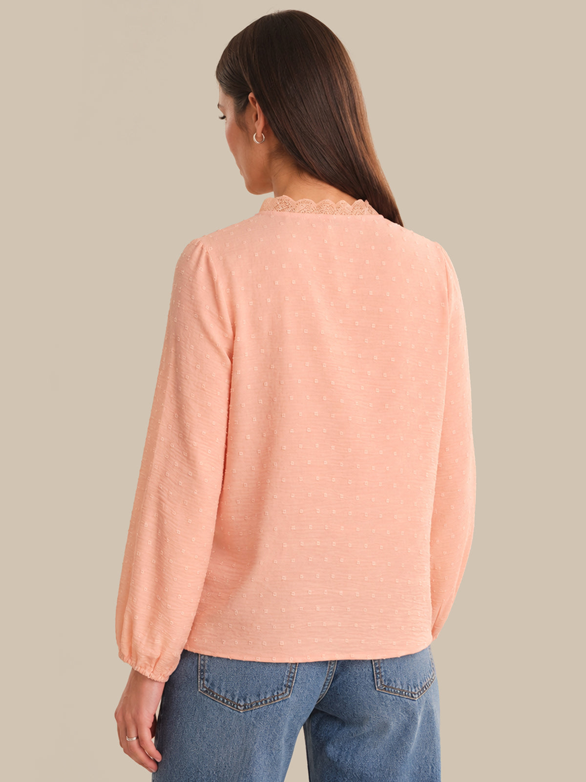 Person wearing a pink sweater and blue jeans on a beige background