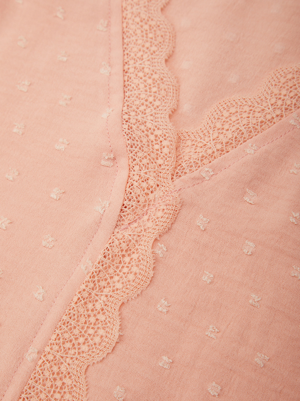 Close-up of a pink fabric with lace trim and floral patterns.