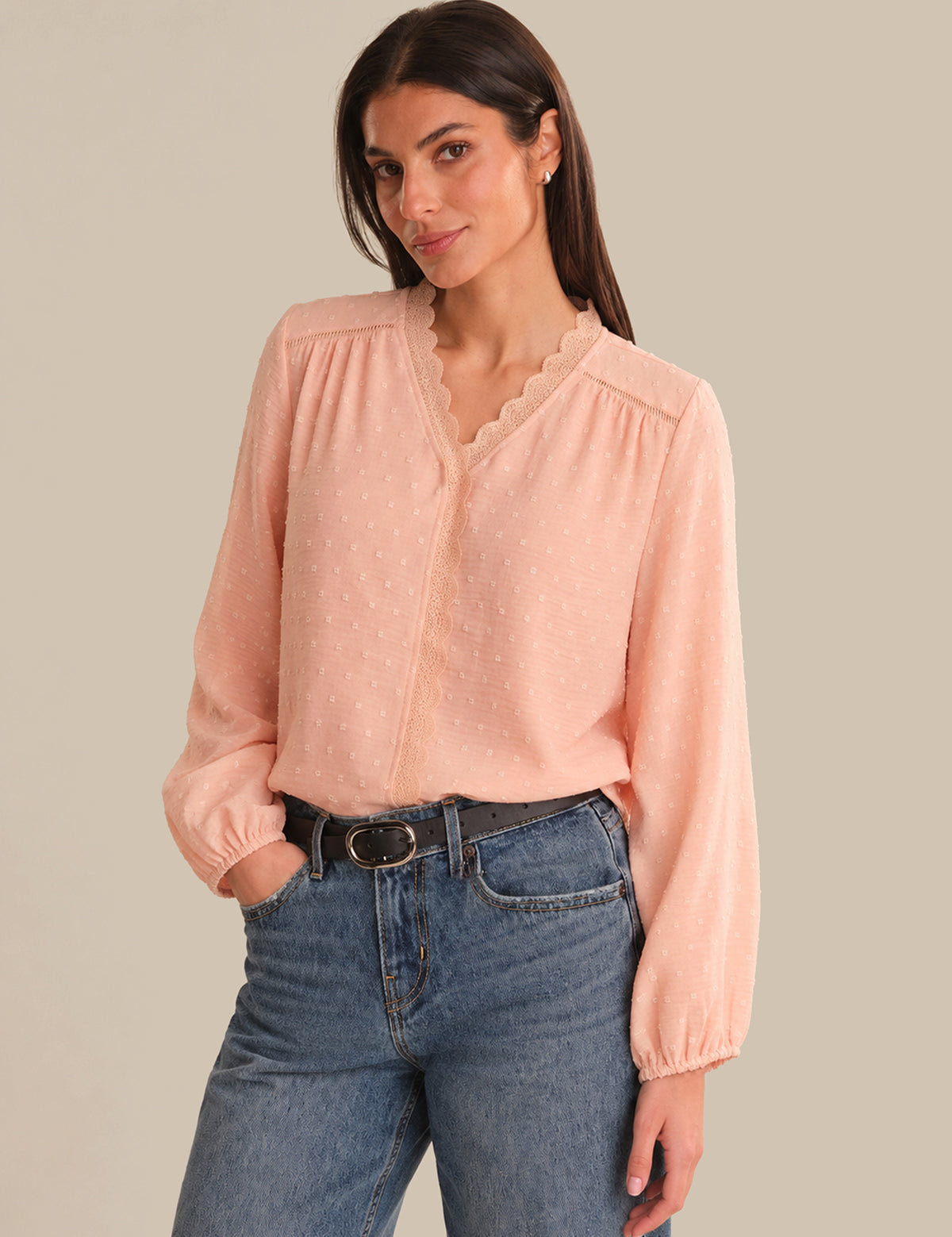 Woman wearing a light pink blouse and blue jeans against a beige background