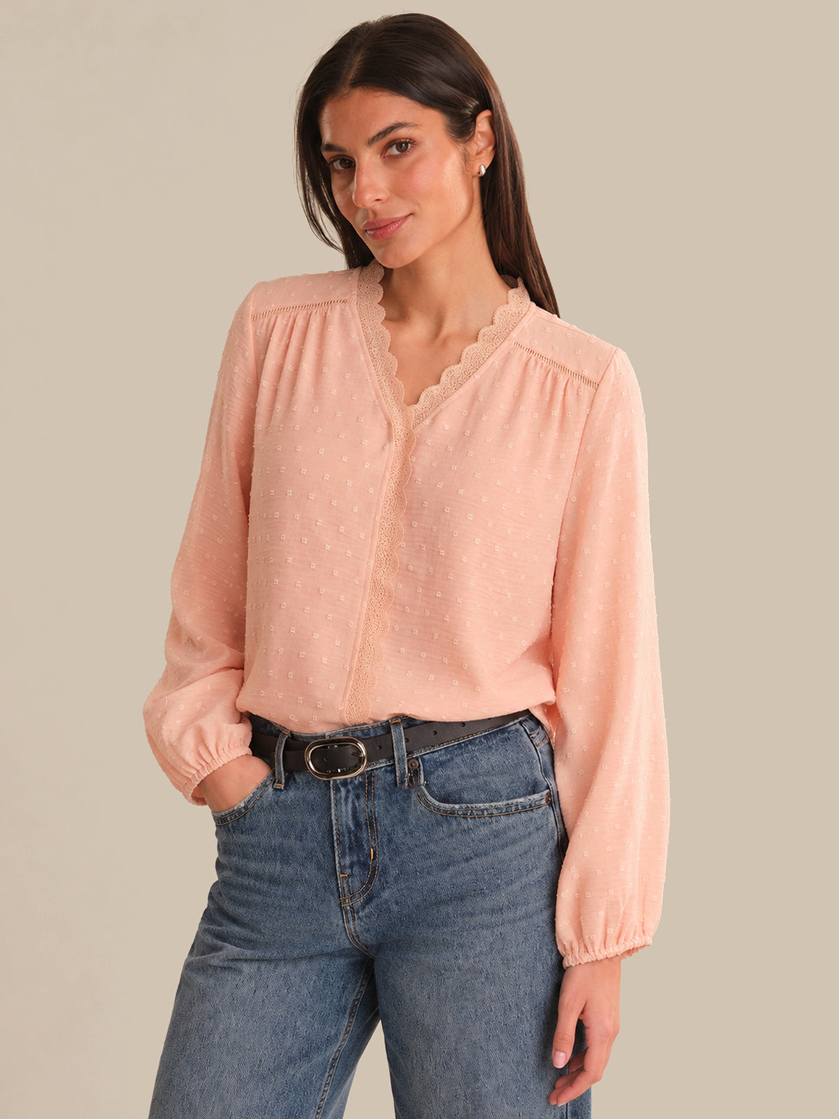 Woman wearing a light pink blouse and blue jeans against a beige background