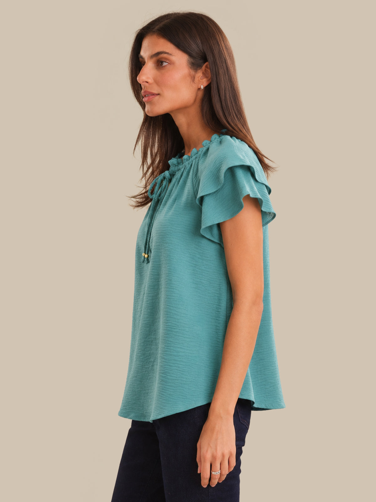 Woman wearing a teal blouse with ruffled sleeves on a beige background