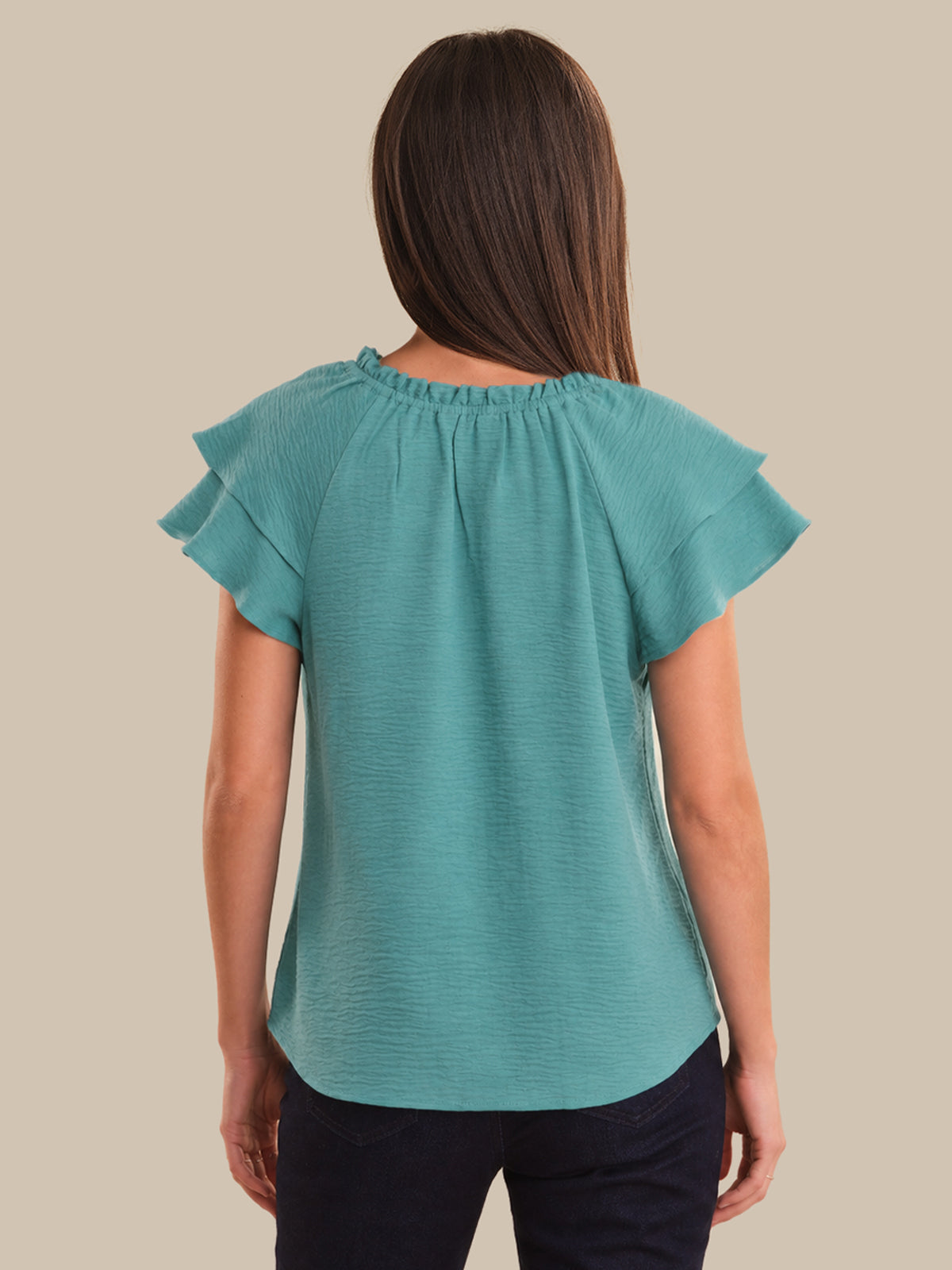 Woman wearing a teal blouse with ruffled sleeves on a beige background