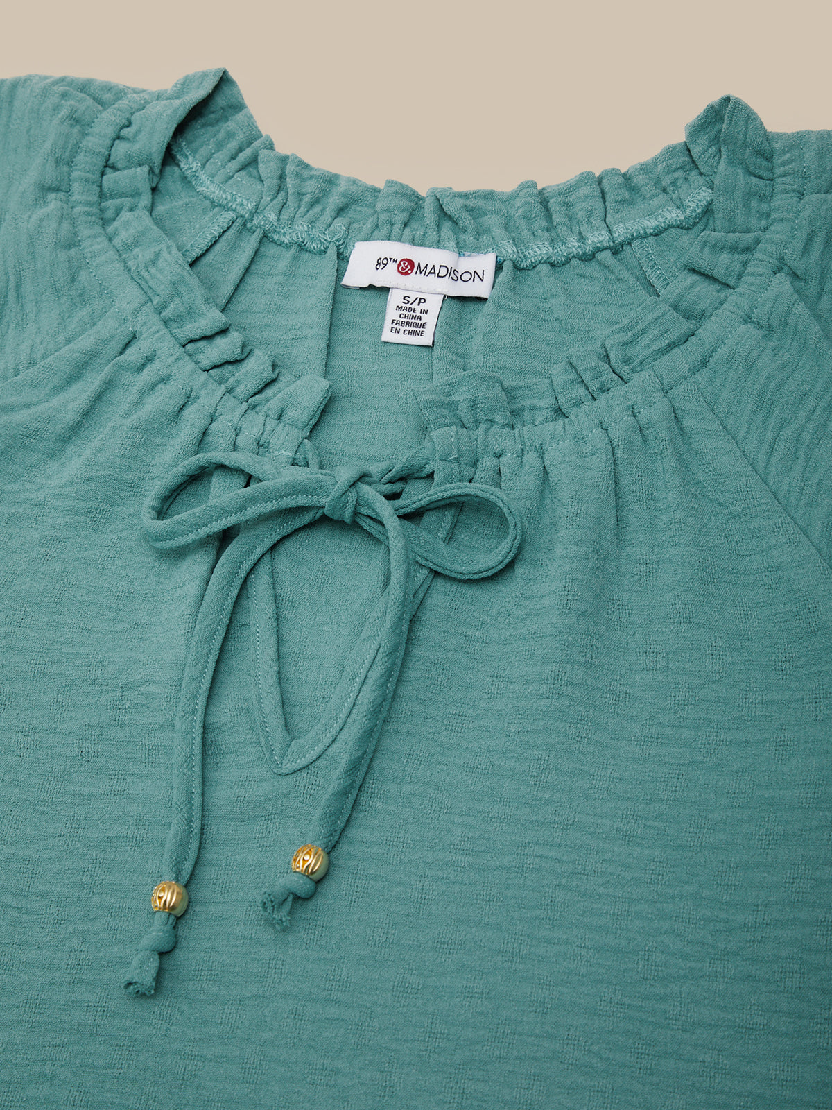 Teal top with ruffled neckline and tie detail, brand label visible.