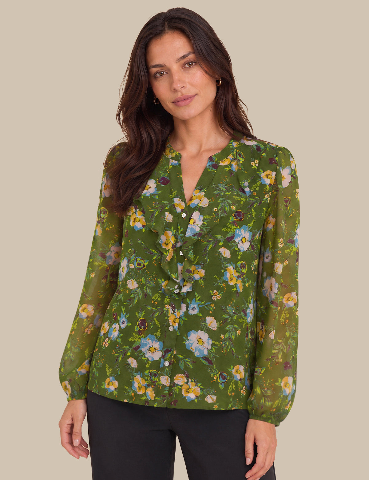 A woman wearing a green long-sleeve blouse with a yellow, blue, and white floral print, paired with black pants, against a solid beige background.