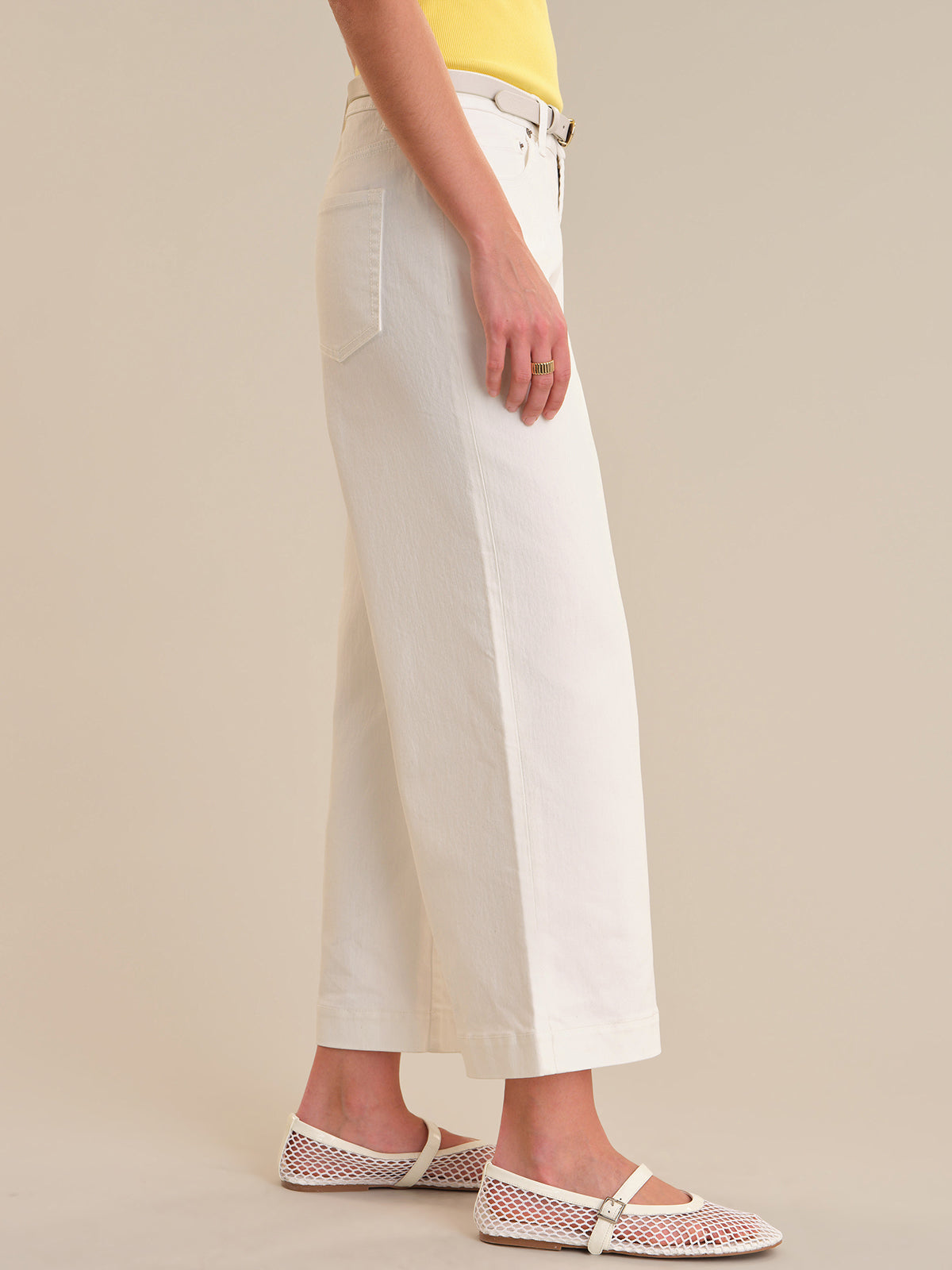 Person wearing white pants and fishnet sandals on a beige background