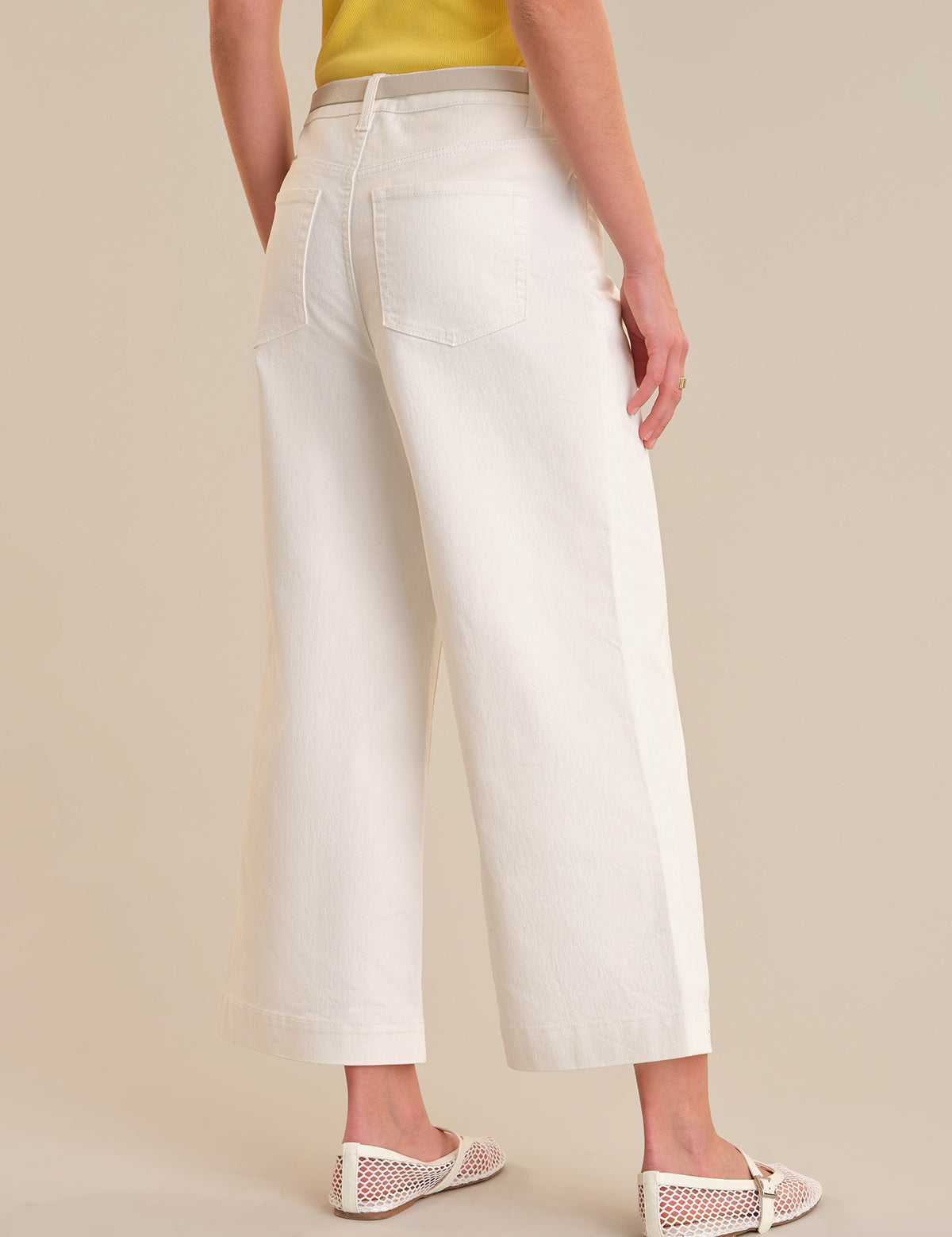 Person wearing white wide-leg pants on a beige background