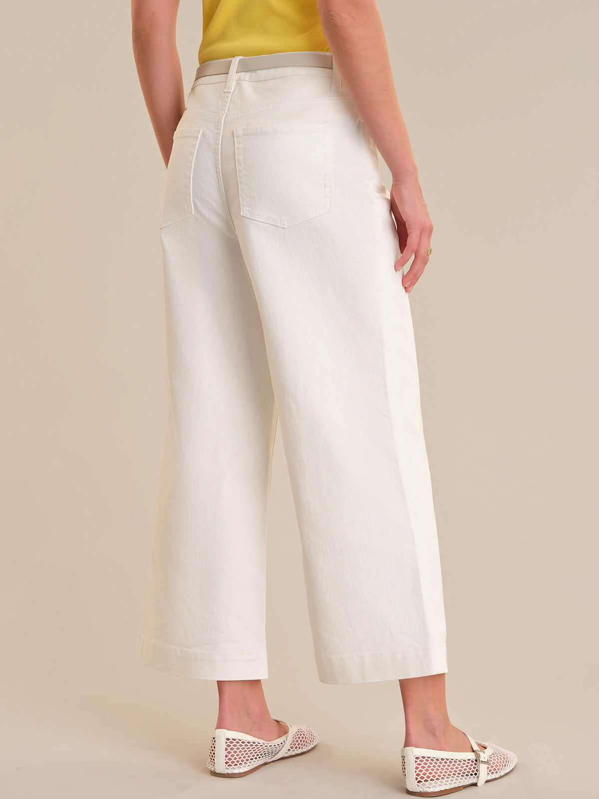 Person wearing white wide-leg pants on a beige background