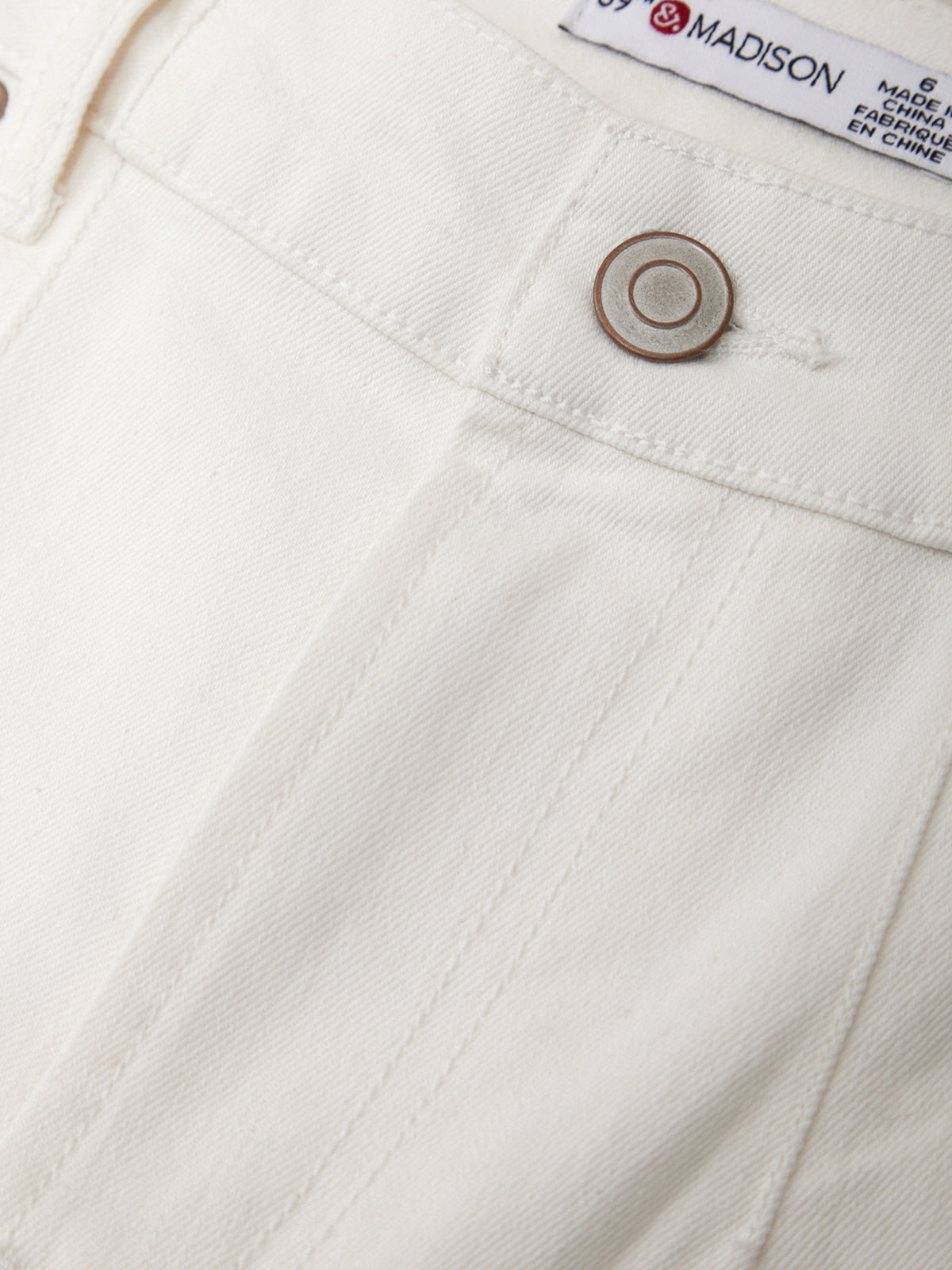 Close-up of a white denim pocket with a button and 'Madison' brand label.