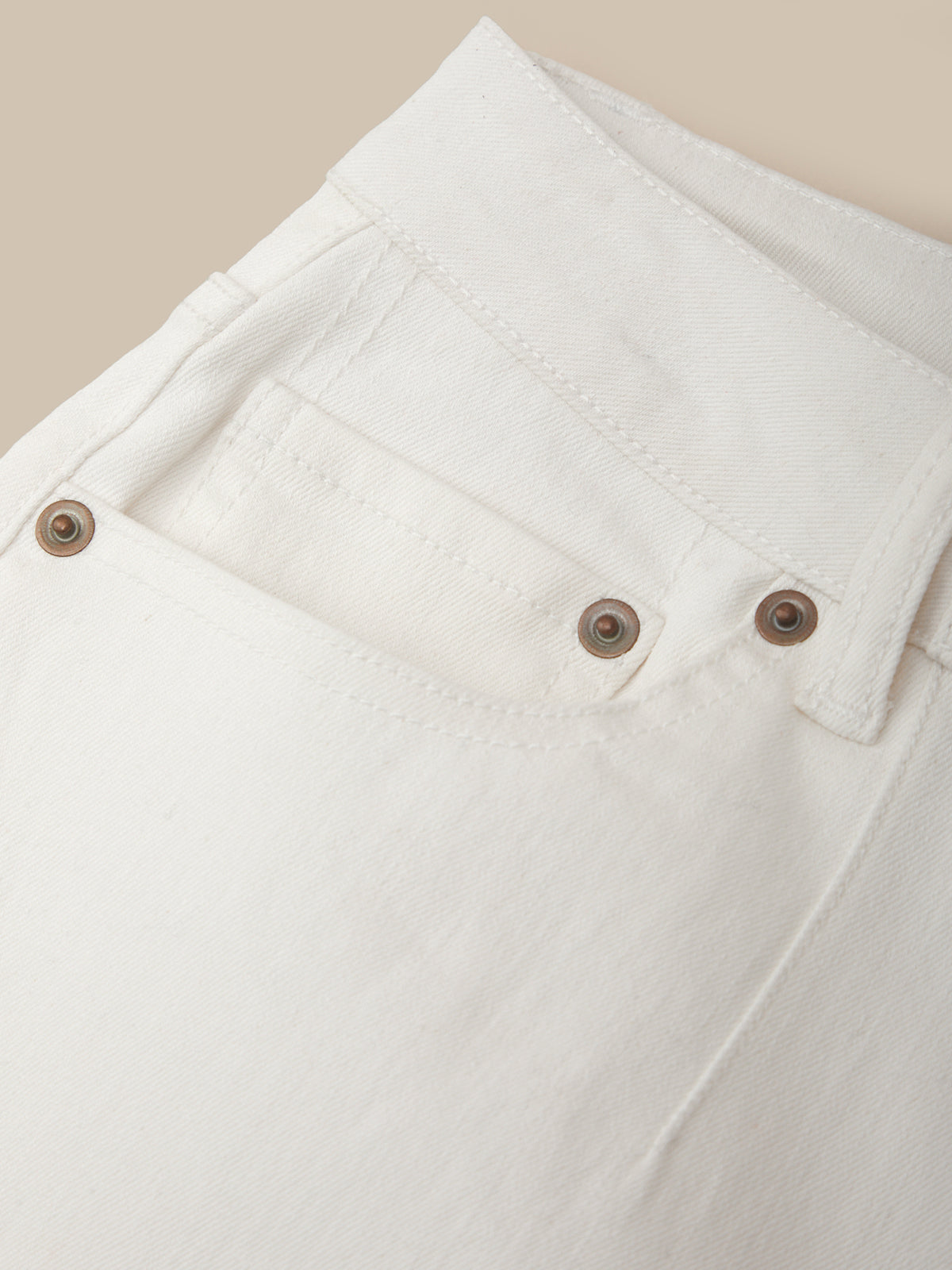 Close-up of a white denim jacket with brown buttons on a beige background