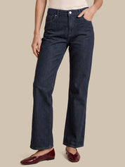 A model wearing dark blue straight-leg denim jeans, styled with a cream top and burgundy flats, against a solid beige background.
