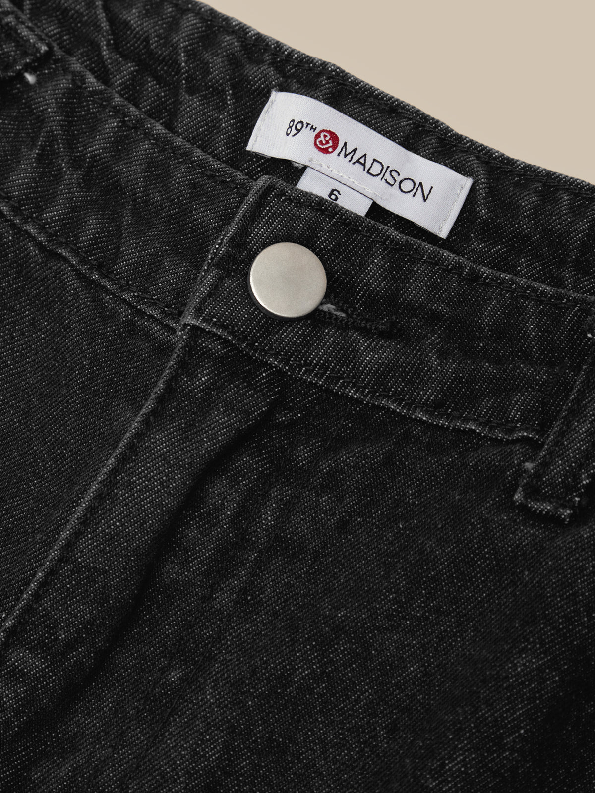 Close-up of a pair of black denim jeans showing the waistband, a white brand label reading Madison, and a silver metal button.