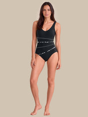 A woman modeling a black one-piece swimsuit with white abstract line patterns, standing against a solid beige background.