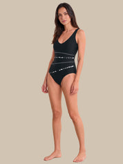 A woman modeling a black one-piece swimsuit with white abstract horizontal line patterns, set against a solid beige background.