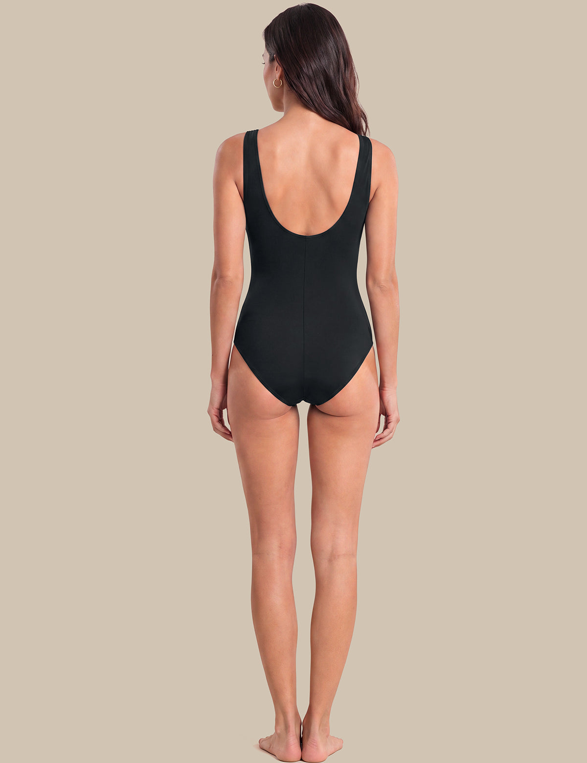 A woman viewed from the back wearing a black one-piece swimsuit, standing against a solid beige background.